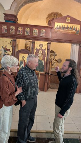 Benjamin Neumann pointing to an the iconostasis before the altar while talking to a couple.